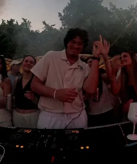 DJ lacht hinter dem Pult, dahinter tanzende Gäste